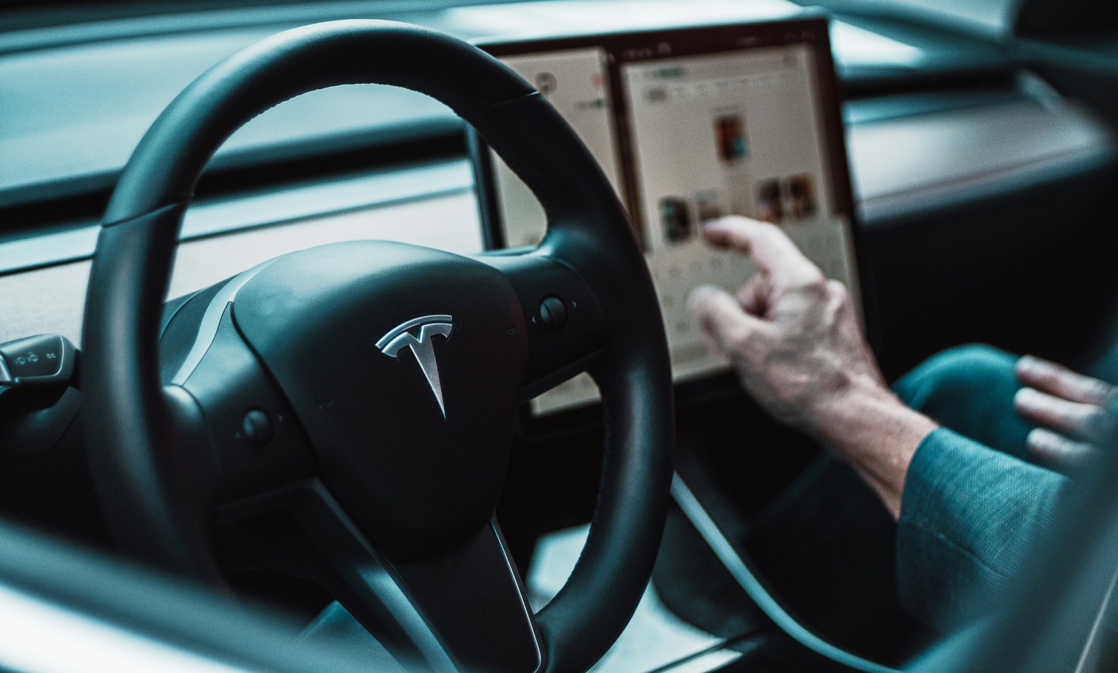 Interior de un Tesla, volante con el logo de la marca y mano tocando la pantalla central