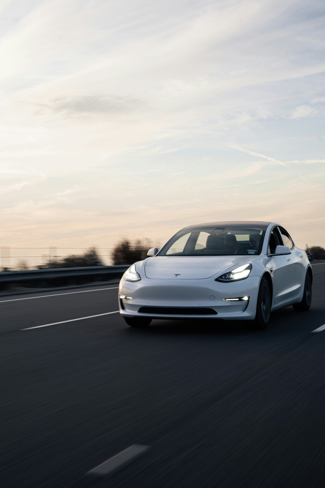 Tesla Model 3 blanco circulando por una ruta al atardecer
