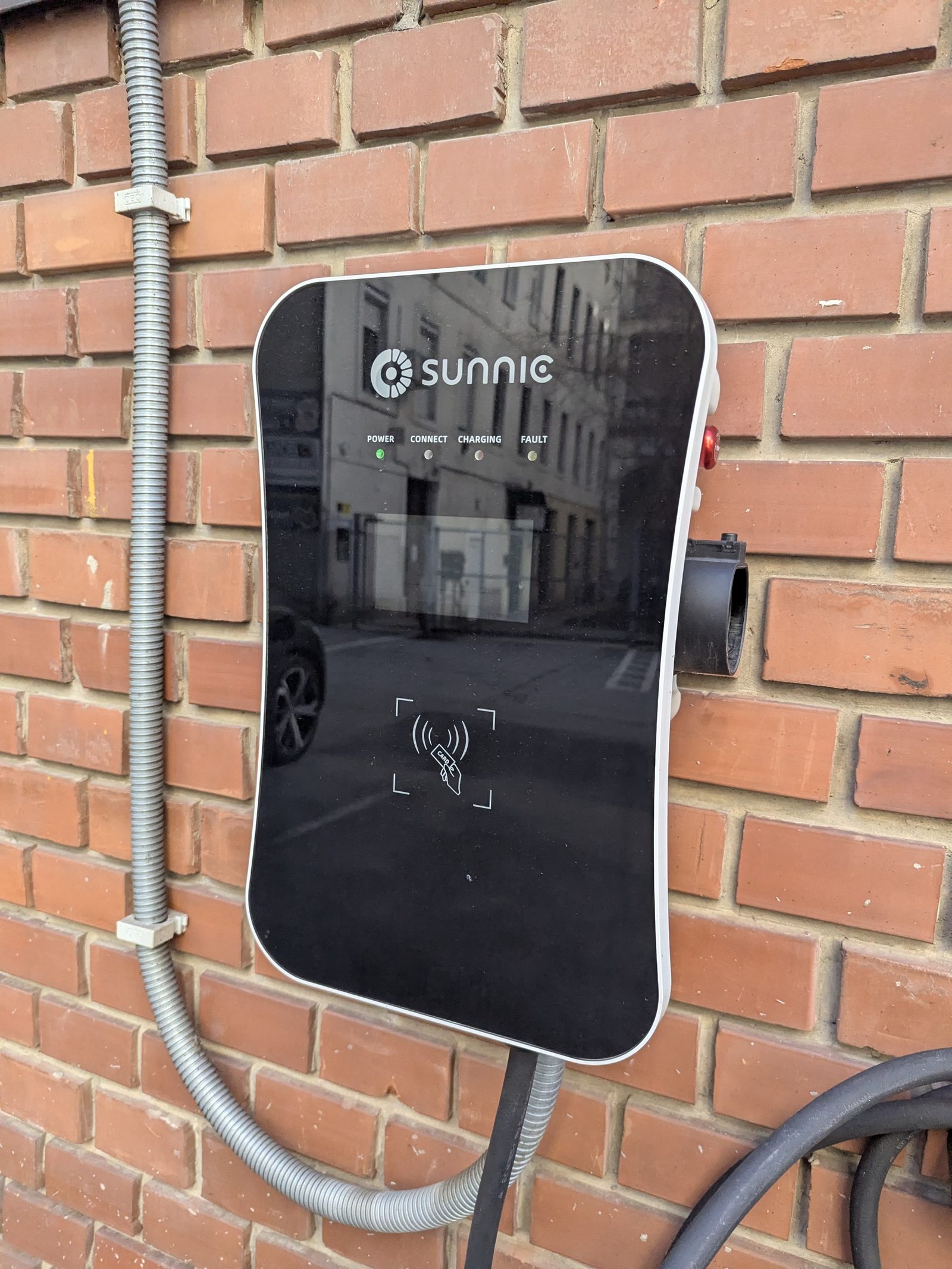 Wallbox Sunnic instalado sobre una pared de ladrillo, con lector de tarjeta RFID, luces de estado y el conector guardado en su soporte