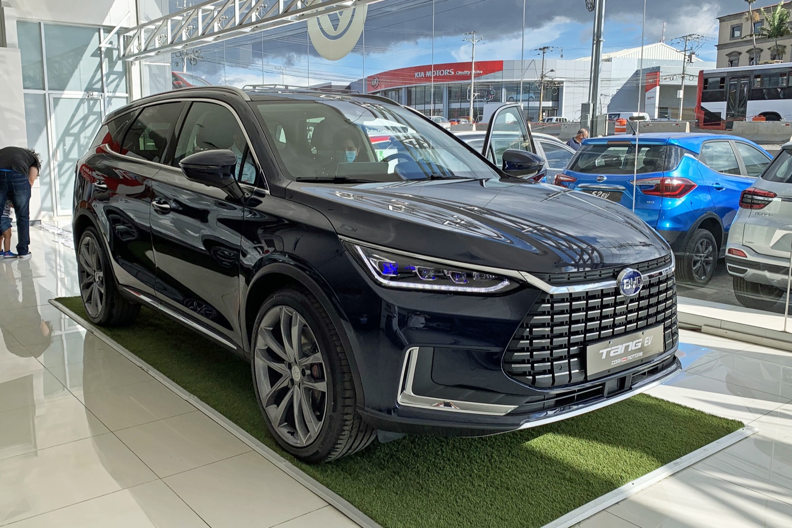BYD Tang EV azul oscuro en un salón de ventas, vista frontal tres cuartos