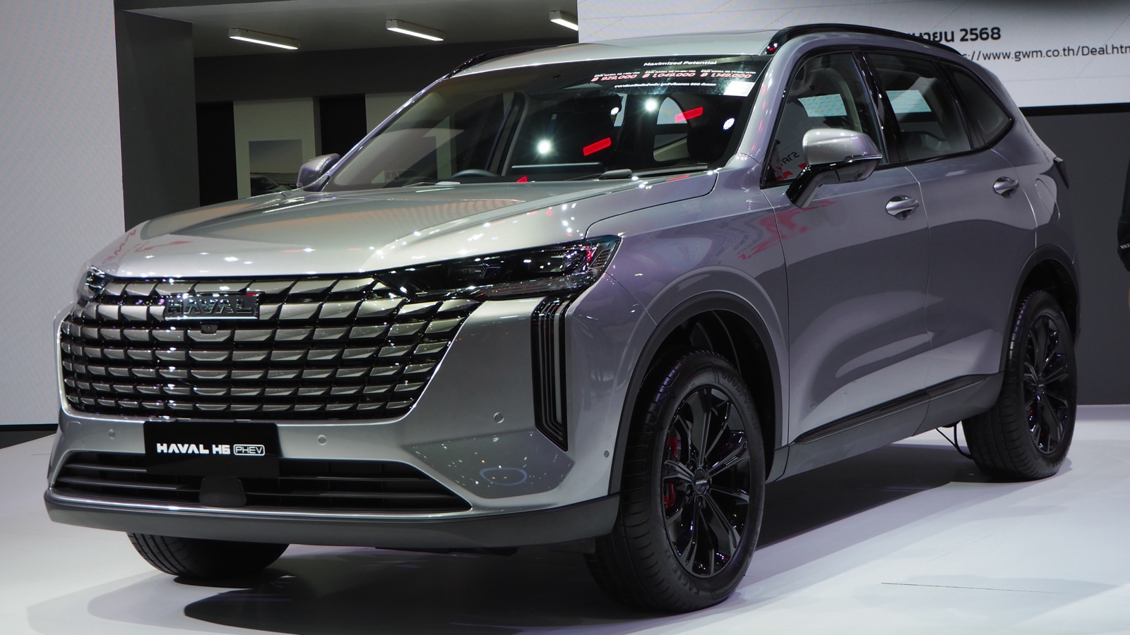 Haval H6 PHEV 2025 gris de frente y tres cuartos, en un salón del automóvil, con la insignia PHEV en el paragolpes